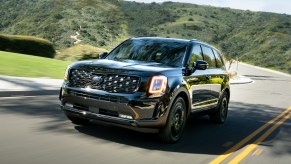 A black 2021 Kia Telluride Nightfall Edition midsize SUV travels on a two-lane through green hills