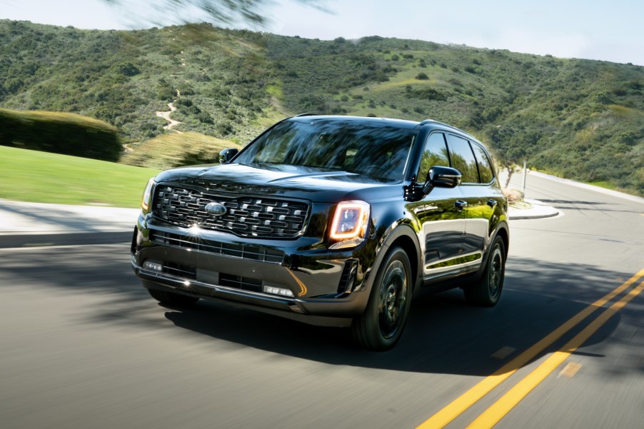 A black 2021 Kia Telluride Nightfall Edition midsize SUV travels on a two-lane through green hills