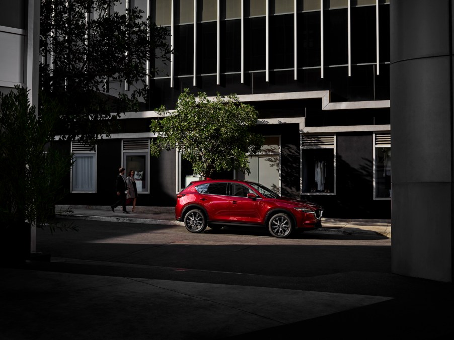 A red metallic 2021 Mazda CX-5 compact SUV parked on a city street as two office workers pass by on a sidewalk