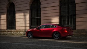 A red 2021 Mazda6 midsize sedan parked along a curb outside a city building