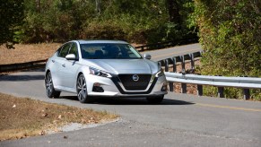 A silver 2021 Nissan Altima midsize sedan traveling on a curvy two-lane highway through trees