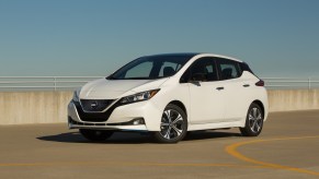 A white 2021 Nissan LEAF SV Plus electric car parked in a lot under a clear blue sky