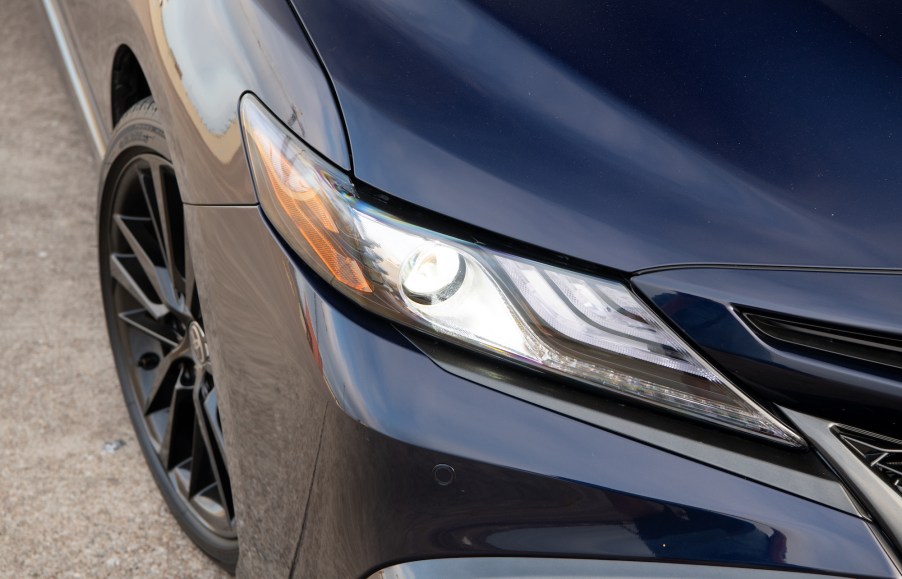 Closeup view of a dark-blue 2021 Toyota Camry XSE sedan's passenger-side hood, headlight, front bumper, and tire