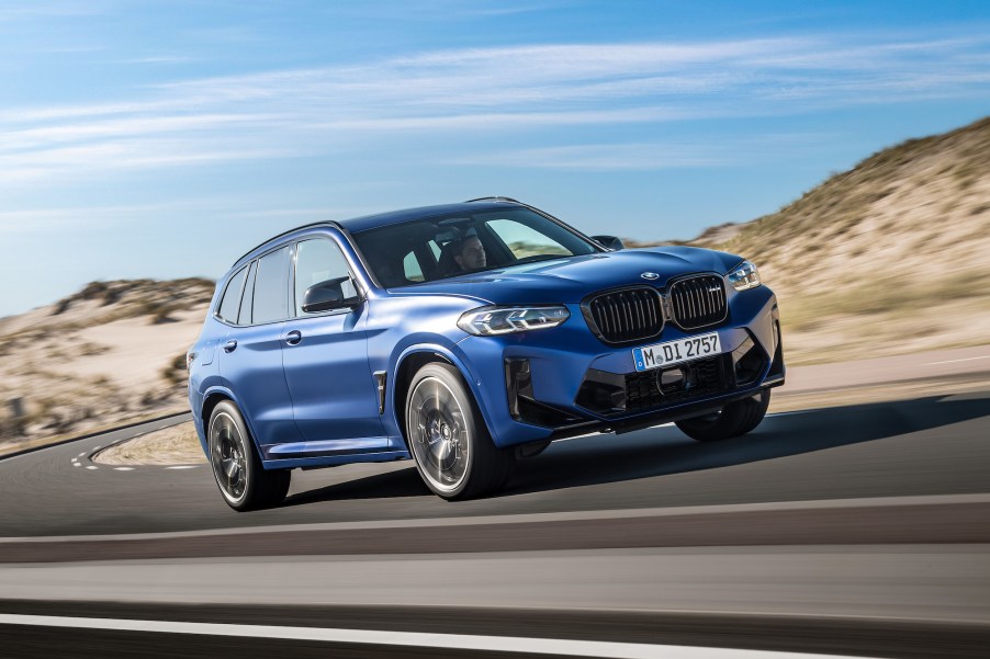 A blue 2022 BMW X3 M Competition luxury compact SUV traveling on a paved road through arid hills