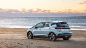 A silver 2022 Chevy Bolt EV hatchback parked on a beach overlooking an ocean as the sun sits below the horizon