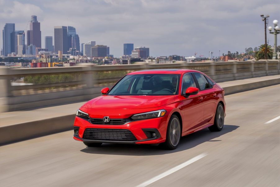 A red 2022 Honda Civic Sedan Touring drives down a city highway