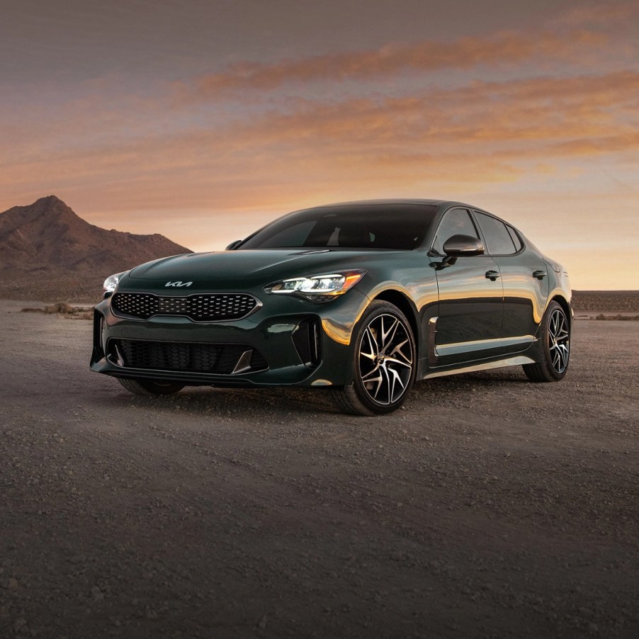 A dark colored 2022 Kia Stinger sits on a dirt road with a small hill behind it.