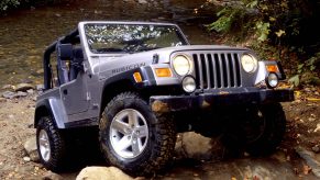 A silver Jeep Wrangler scrabbles up a rock face