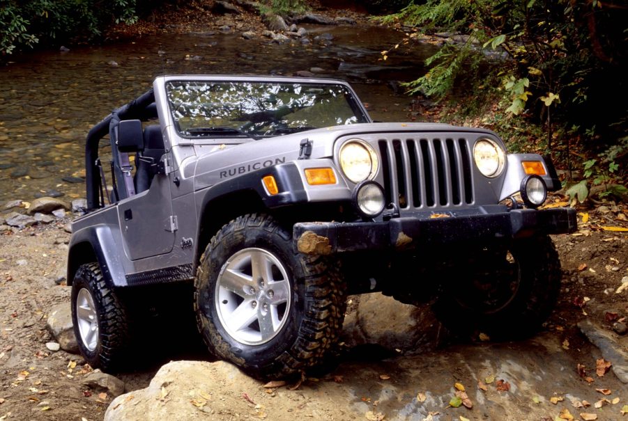 A silver Jeep Wrangler scrabbles up a rock face