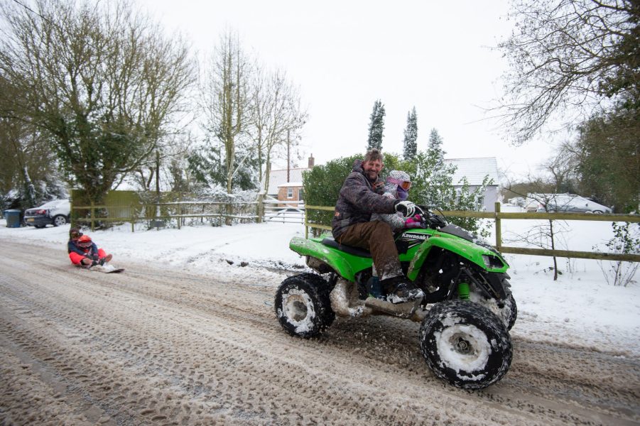 Richard Squirrell uses a quad bike to give his granddaughters a ride in the snow in Wattisham in Suffolk, with heavy snow set to bring disruption to south-east England