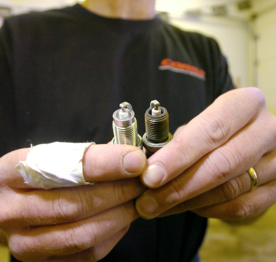 A black-shirted mechanic compares old and new spark plugs while changing them