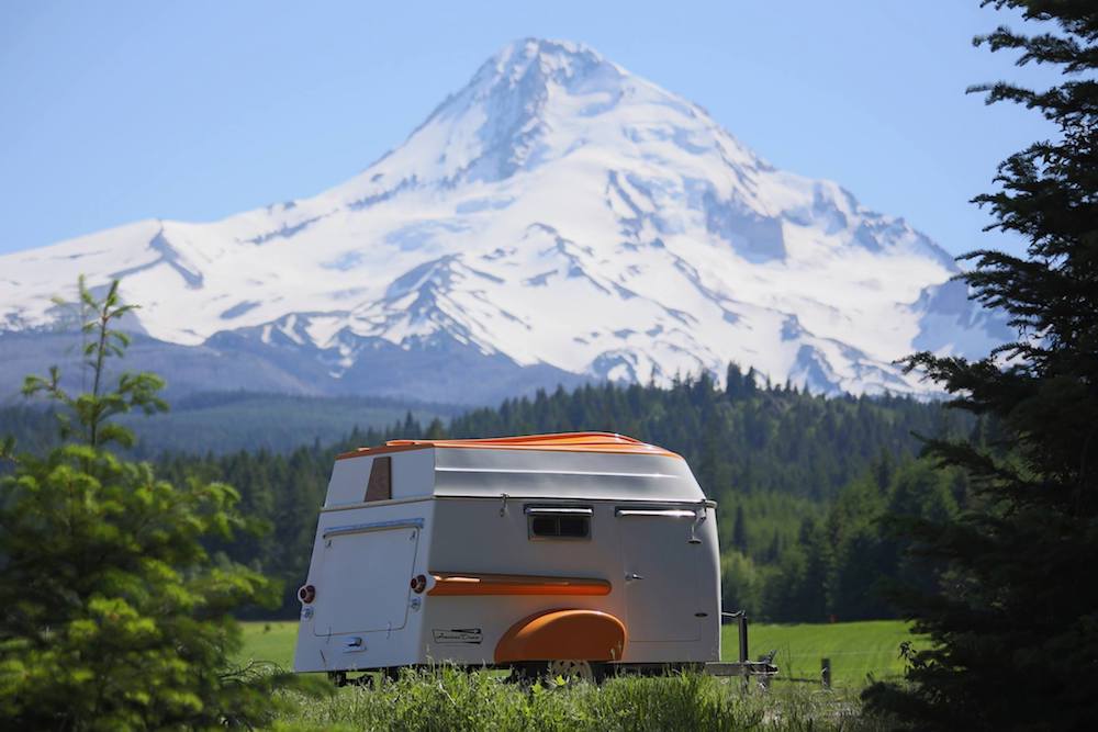 The American Dream trailer parked in a meadow with snowcapped mountains behind 