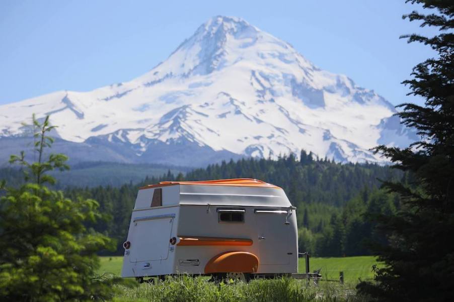 The American Dream trailer parked in a meadow with snowcapped mountains behind