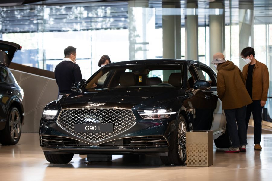 Customers wearing protective masks look at a black Hyundai Motor Co. Genesis G90 L luxury sedan on display at the company's Motorstudio showroom