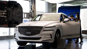 Customers wearing protective masks look at a Hyundai Motor Co. white Genesis GV80 sport utility vehicle (SUV) at the company's Motorstudio showroom in Seoul, South Korea