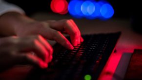 A man types on a keyboard in a dark room, perhaps looking for a used car.