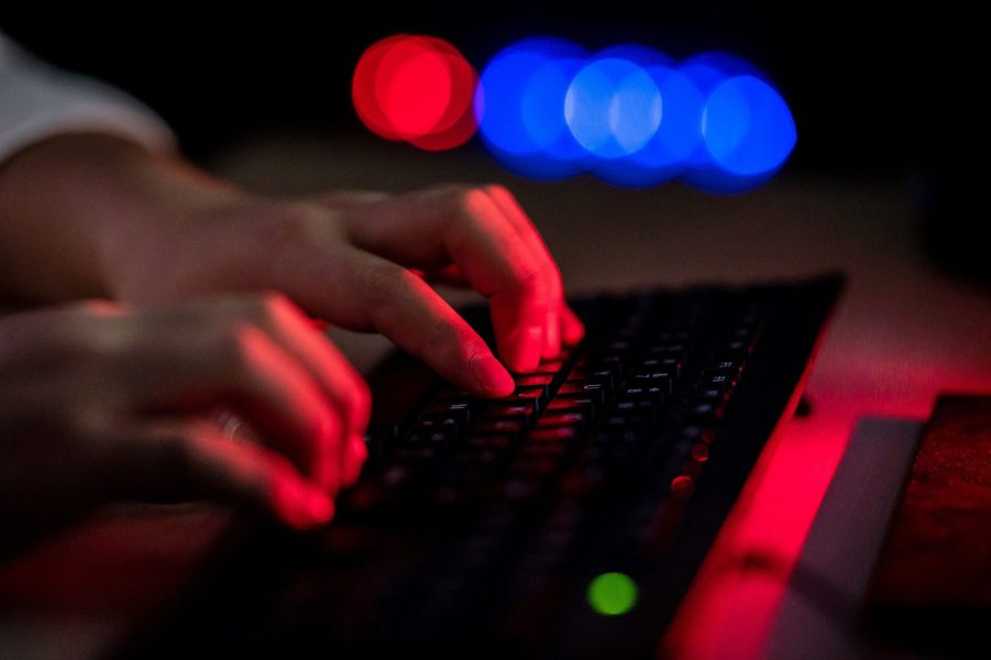 A man types on a keyboard in a dark room, perhaps looking for a used car.