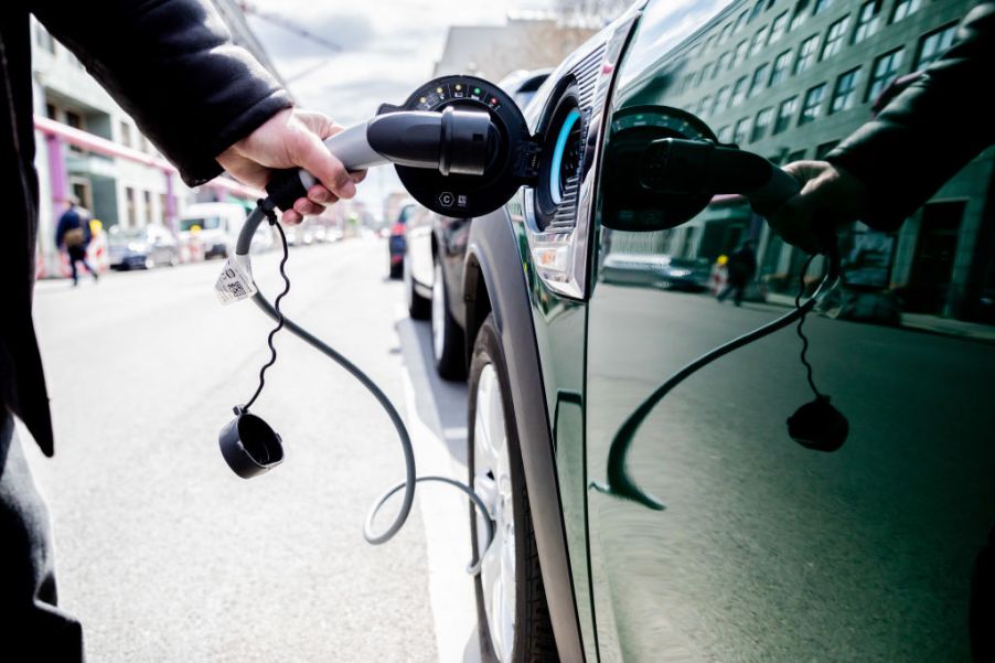 A person plugs an EV charger into a green car