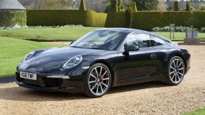 A black Porsche 911 sits on a grass and gravel lawn