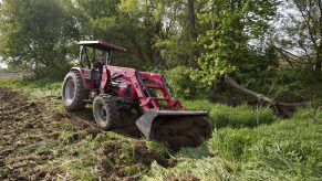 a red mahindra tractor clearing the edge of a corn field in the USA