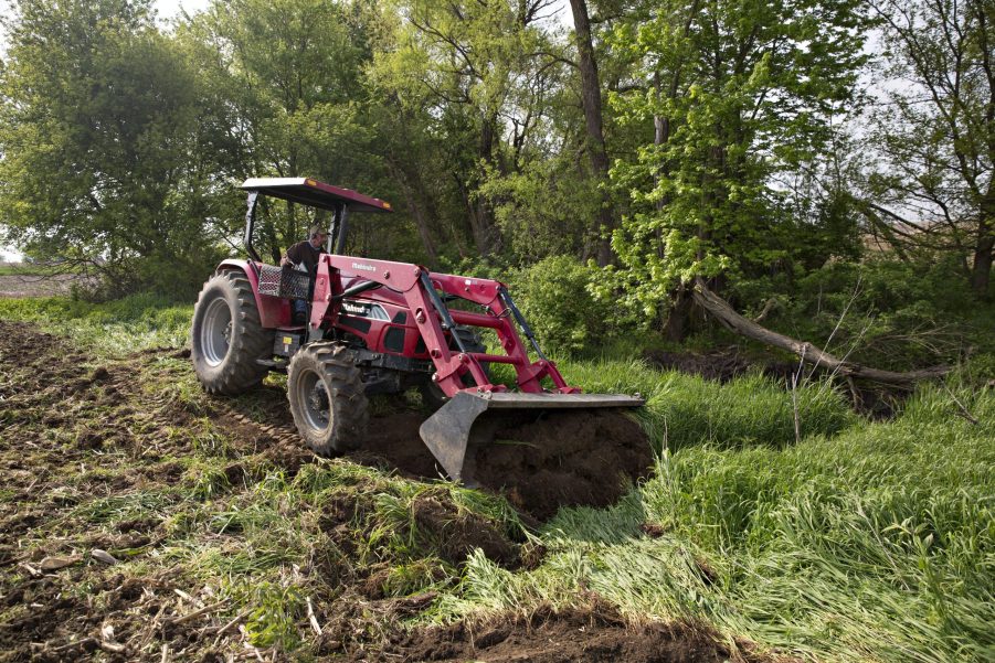 a red mahindra tractor clearing the edge of a corn field in the USA