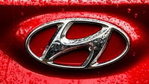 A silver Hyundai emblem on a red car is covered with raindrops