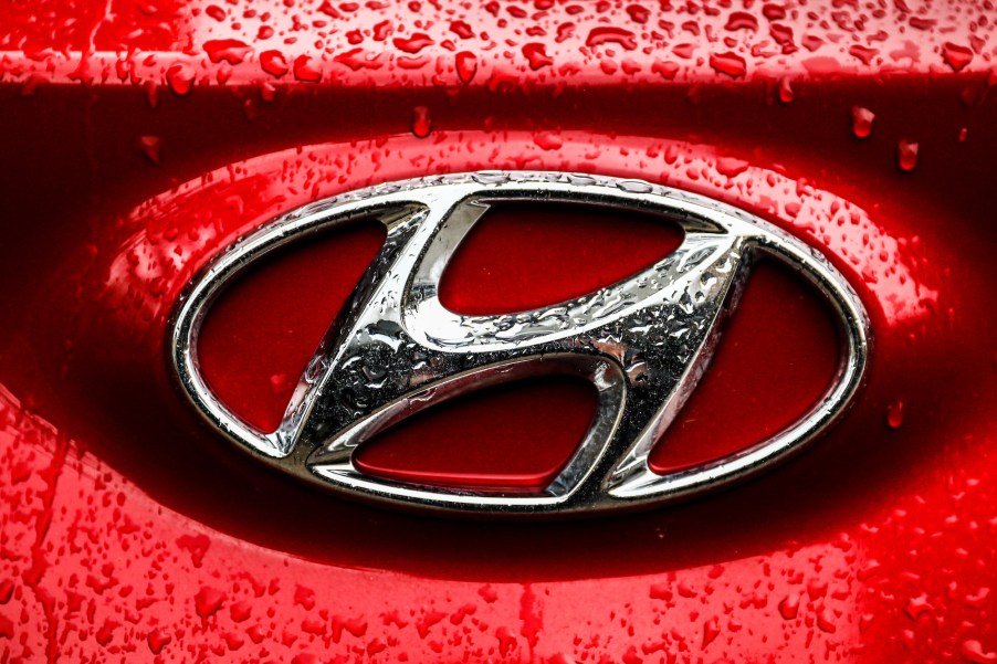 A silver Hyundai emblem on a red car is covered with raindrops