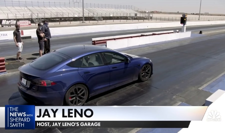 NHRA officials look on as Jay Leno sits on a dragstrip in a blue Tesla Model S Plaid