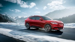 A red 2021 Ford Mustang Mach-E drives down a snow-lined road.