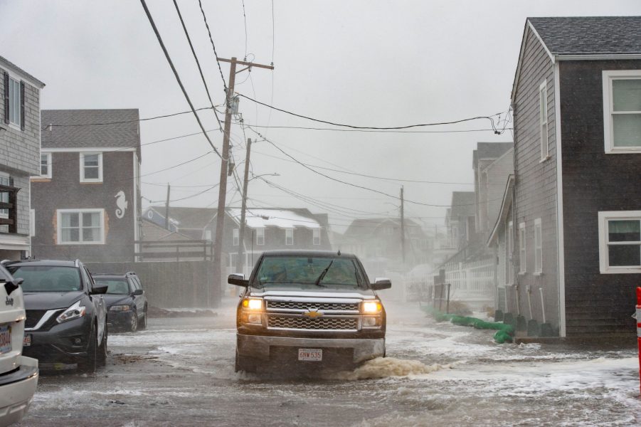 A truck drives through a flooded street as waves crash over the sea walls during high tide in a winter storm in Scituate, Massachusetts