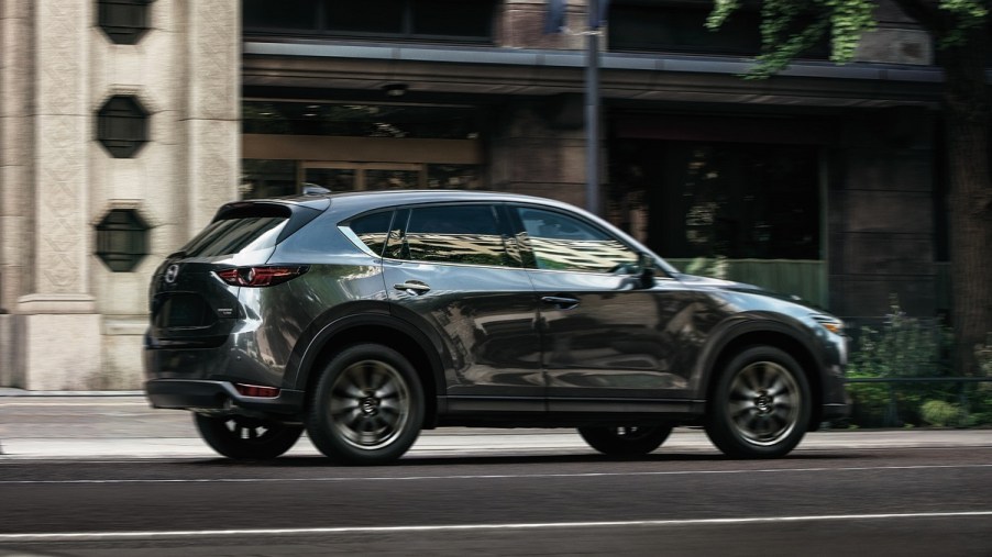 A dark colored Mazda CX-5 drives through a city.