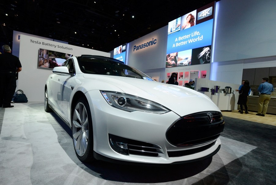 A white Tesla electric car on display at a Panasonic booth at a car show.