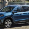 A blue 2021 Honda Pilot parked at a lake while a girl fishes in the background.