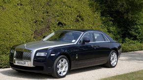 A black and silver Rolls-Royce Ghost luxury sedan parked in front of a tall hedge