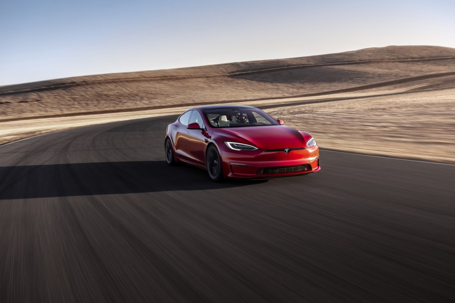 A red Tesla Model S Plaid sedan drives on a curving road in a desert