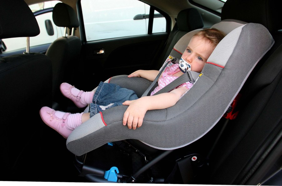 A small child in a foward-facing car seat in a vehicle's backseat