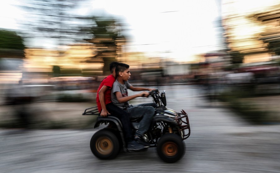 Two kids without helmets ride an ATV