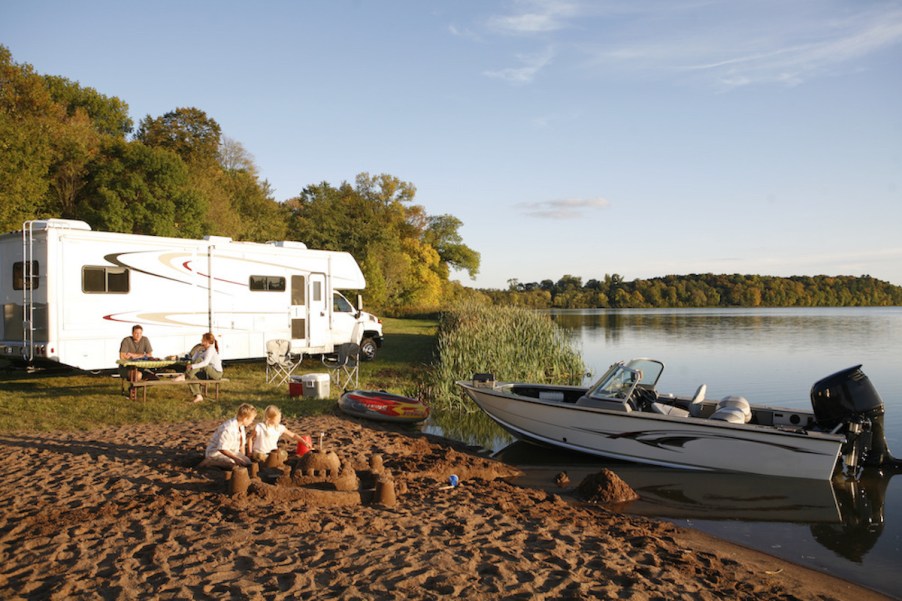 an RV camper and a small boat camping set up next to a lake