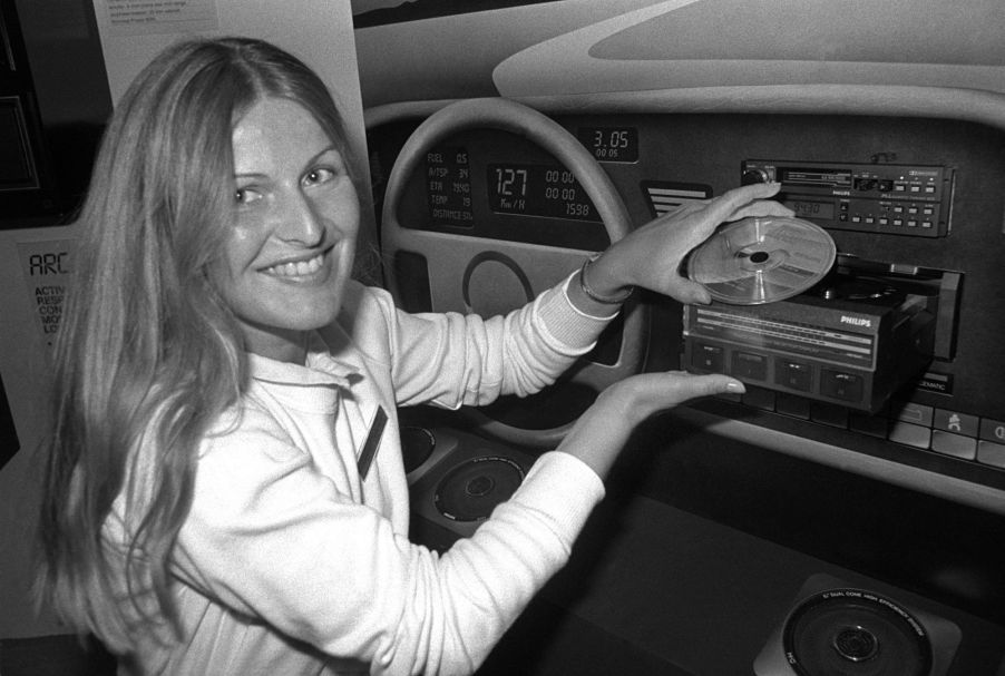 A black and white photo of a woman presenting a CD player in a vehicle