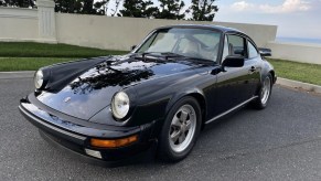 The front 3/4 view of a black 1984 Porsche 911 Carrera 3.2 parked in an oceanside parking lot