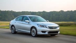 A silver 2015 Honda Accord Hybrid EX-L driving, the 2015 Honda Accord Hybrid is the best used hybrid under $20,000