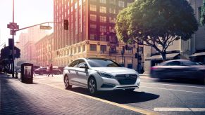 A silver gray 2016 Hyundai Sonata Hybrid model parked next to a cobblestone walking path