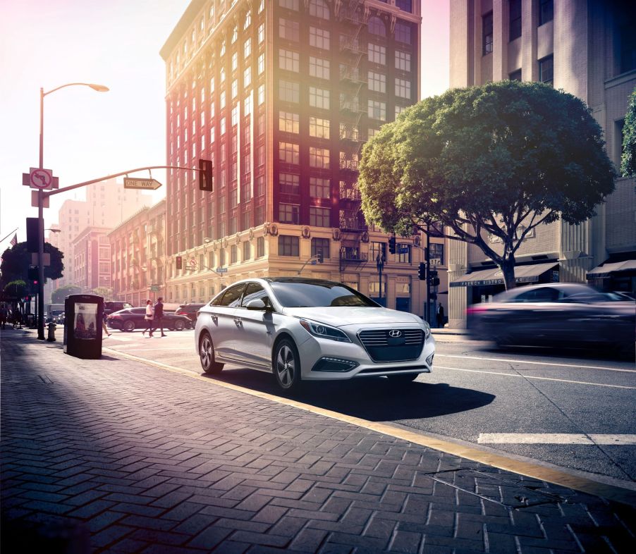 A silver gray 2016 Hyundai Sonata Hybrid model parked next to a cobblestone walking path