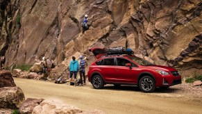 A red 2017 Subaru Crosstrek Special Edition parked at the bottom of a rocky cliff as a climber scales it