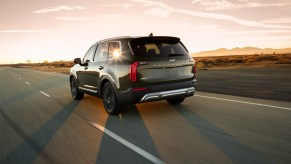 A dark-green 2020 Kia Telluride midsize SUV on a highway road trip through a desert