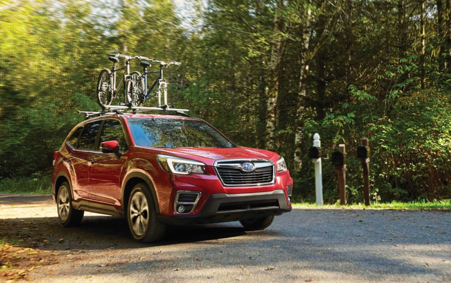 A red 2020 Subaru Forester in a wooded area parked on a dirt road with bicycles on the top rack.