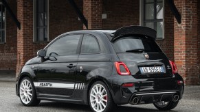 The rear 3/4 view of a black-and-white 2021 Abarth 695 EsseEsse next to a brick building