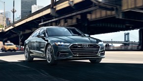 A dark grey 2021 Audi A7 AWD sedan driving underneath a bridge in the middle of a city