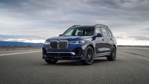 A blue 2021 BMW Alpina XB7 parked on a blacktop area with a cloudy sky in the background.