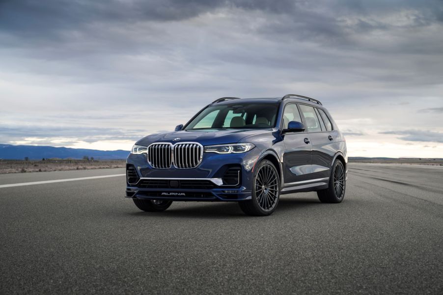 A blue 2021 BMW Alpina XB7 parked on a blacktop area with a cloudy sky in the background.